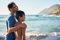 Liebevolle Umarmung von Vater und Sohn am sonnigen Ozeanstrand — Stockfoto