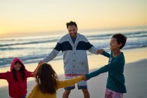 Feliz padre e hijos tomados de la mano en círculo en la playa puesta del sol - foto de stock