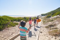 Hermanos y hermanas corriendo en el soleado paseo marítimo de la playa - foto de stock
