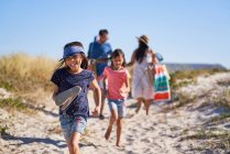 Счастливая девочка бегает по солнечному пляжу с семьей — стоковое фото