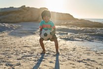 Retrato bonito menino jogando com bola de futebol na praia ensolarada — Fotografia de Stock