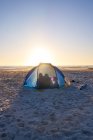 Silhouette famiglia all'interno tenda sulla spiaggia soleggiata tramonto — Foto stock