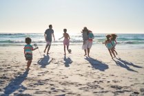 Família correndo e jogando futebol na praia do oceano ensolarado — Fotografia de Stock