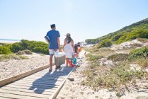 Family carrying equipment on sunny beach boardwalk — Stock Photo