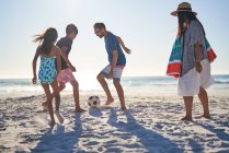 Familia jugando al fútbol en la soleada playa del océano - foto de stock