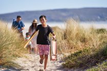 Niño feliz corriendo con silla plegable en camino de playa soleado - foto de stock