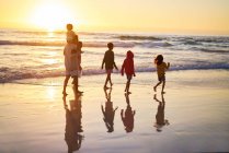 Familia caminando en el océano surf en la playa al atardecer - foto de stock
