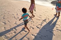 Lindo chico corriendo en la playa con la familia - foto de stock