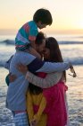 Прихильна сім'я обіймається на океанічному пляжі на заході сонця — стокове фото