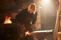 Female blacksmith forging steel in workshop — Stock Photo