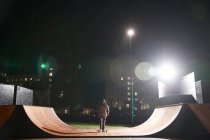 Young man skateboarding on ramp at skate park at night — Stock Photo