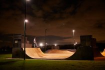 Young man skateboarding on skate park ramp at night — Stock Photo