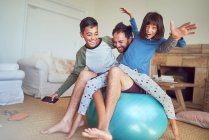 Retrato familia feliz jugando en la pelota de fitness en la sala de estar - foto de stock
