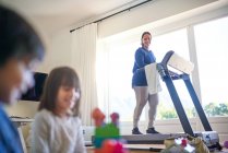 Mother exercising on treadmill and watching kids play — Stock Photo