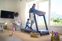 Kids running around mother exercising on treadmill — Stock Photo