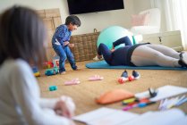 Playful boy watching mother exercise on living room floor — Stock Photo