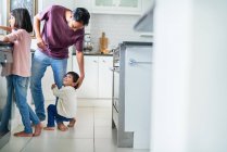 Menino afetuoso abraçando perna de pai na cozinha — Fotografia de Stock