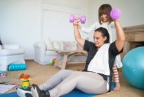 Daughter helping mother exercising with dumbbells in living room — Stock Photo