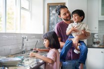 Pai feliz e crianças fazendo pratos na pia da cozinha — Fotografia de Stock