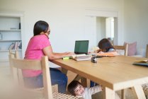 Mother working at laptop with kids playing and doing homework — Stock Photo