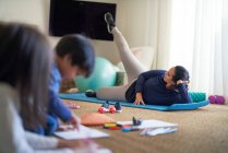Mother exercising in living room with kids coloring nearby — Stock Photo