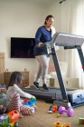 Mother exercising on treadmill while daughter plays on floor — Stock Photo