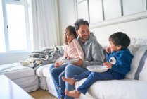 Père heureux et les enfants mangent du pop-corn sur le canapé du salon — Photo de stock