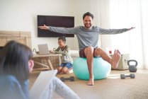 Padre juguetón haciendo ejercicio en la pelota de fitness en la sala de estar con los niños - foto de stock