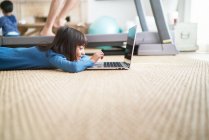 Дівчина використовує ноутбук на підлозі у вітальні поруч з батьком на біговій доріжці — стокове фото