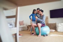 Padre e hijos usando un teléfono inteligente y haciendo ejercicio en la sala de estar - foto de stock