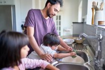 Отец и дети моют посуду у кухонной раковины — стоковое фото