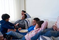 Family relaxing and eating popcorn on living room sofa — Stock Photo