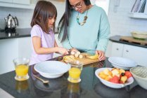Mother helping daughter cut banana in kitchen — Stock Photo