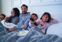 Сім'я відпочиває на дивані і дивиться телевізор з попкорном — стокове фото
