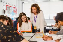 Вчителька середньої школи допомагає студенту-дівчинці навчатися за столом у класі — стокове фото