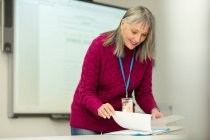 Lächelnde Lehrerin mit Papierkram bei der Vorbereitung im Klassenzimmer — Stockfoto