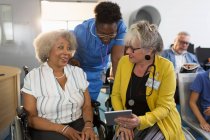 Жінка-лікар з цифровим планшетом розмовляє зі старшим пацієнтом у інвалідному візку у вітальні клініки — стокове фото