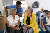 Женщина-врач с цифровым планшетом разговаривает со старшим пациентом в инвалидном кресле в холле клиники — стоковое фото