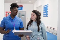 Female doctor and nurse making rounds, discussing medical chart in hospital corridor — Stock Photo