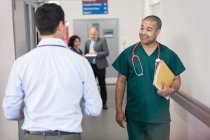 Smiling male surgeon greeting passing doctor in hospital corridor — Stock Photo