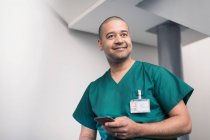 Cirurgião masculino sorridente usando telefone inteligente — Fotografia de Stock
