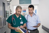 Чоловік лікар і хірург обговорюють медичну карту, роблячи раунди в лікарняному коридорі — стокове фото
