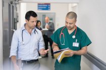 Чоловік лікар і хірург обговорюють медичну карту, роблячи раунди в лікарняному коридорі — стокове фото