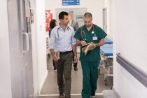 Чоловік лікар і хірург з медичною картою роблять раунди в лікарняному коридорі — стокове фото