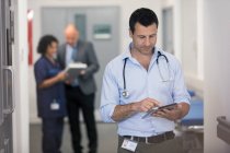 Чоловік лікар використовує цифровий планшет в лікарняному коридорі — стокове фото