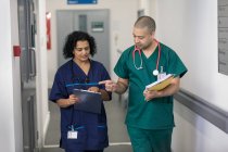 Лікар і хірург обговорюють медичну карту, роблячи раунди в лікарняному коридорі — стокове фото