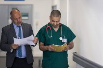 Male administrator and surgeon reading paperwork in hospital corridor — Stock Photo