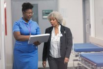 Женщина-врач и медсестра обсуждают медицинскую карту, совершают обход в больничном коридоре — стоковое фото
