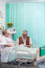 Homem sênior com cartão de visita esposa visitante descansando no quarto do hospital — Fotografia de Stock