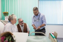 Médico com tablet digital fazendo rondas, conversando com casal de idosos no quarto do hospital — Fotografia de Stock